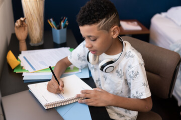 Young boy studies and writes at the table in his room