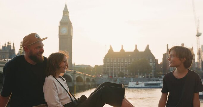 Happy family of father and two teenager talk and laugh together with stunning views of London in beautiful sunlight
