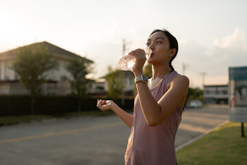 Confident young Asian woman running outdoors along village street. Stand and drink water to cool...