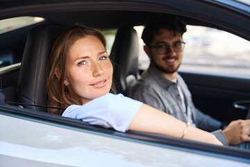 Fototapeta na wymiar Young smiling caucasian woman and blurred man looking at camera from car window
