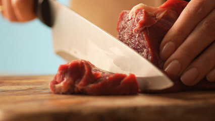Slicing Raw Beef on Wooden Board. Close-up, shallow dof.