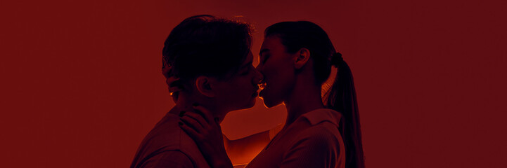 Passionate young man and woman, young couple kissing, expressing love against red background in...