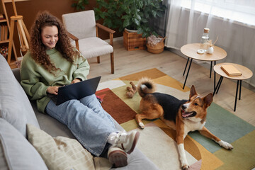 High angle portrait of young woman relaxing on couch with dog waiting happily on floor, copy space