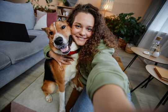 POV of young woman taking selfie photo with happy dog at home, copy space