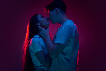 Boyfriend and girlfriend, young man and woman kissing against purple background in neon light....