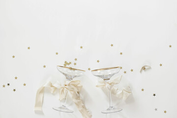 Champagne glasses with golden star shaped confetti tinsel on white table background. Celebrate,...