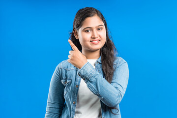Portrait of a happy gorgeous Indian women specifies with forefinger to upwards, isolated on blue background - obrazy, fototapety, plakaty