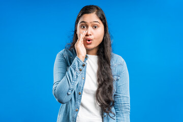 indian women gossiping secretly with covering mouth with hand in blue background