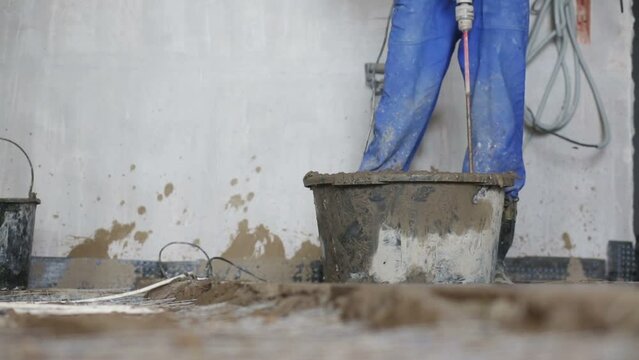 Legs and drill of worker preparing concrete mixture 