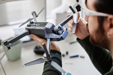 Close up of unrecognizable man holding drone with action camera in tech repair workshop, copy space