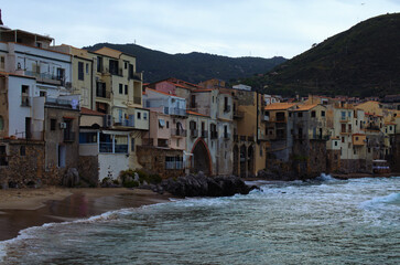 Scenic coastline view of ancient city Cefalu. Colorful buildings at the sandy beach. Waves of tranquil water splashing against the walls. The Tyrrhenian Sea, Cefalu, Sicily, Italy