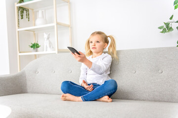 Blond girl holding remote control on sofa at home