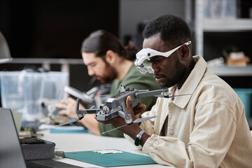 Side view portrait of African American man fixing quadcopter drone at workstation in tech repair...