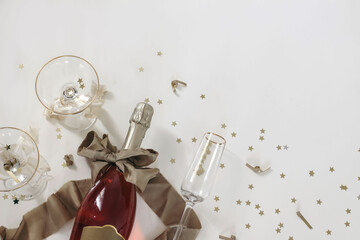 New years Eve holiday corner, banner. Bottle of champagne rose wine, glasses. Golden bow, star shape confetti isolated on white table background. Birthday, party celebration. Alcohol drink. Flat lay