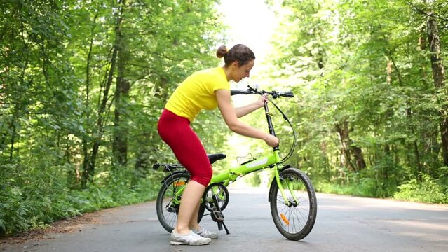 Young woman raises seat and steering wheel of bike and rides