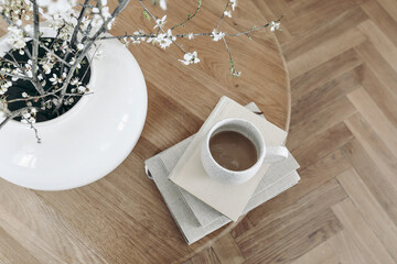 Spring breakfast scene. Cup of coffee on books. Round oak coffee table. Blurred parquet floor....