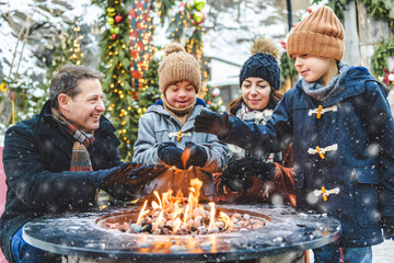 family with two little son having fun together outdoor on frosty day close to a fire