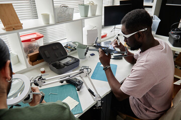 Side view portrait of African American man fixing quadcopter drone while working in electronics...