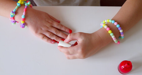 Little girl make manicure and painting nails with red nail polish at home. - obrazy, fototapety, plakaty