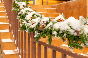 Christmas street decor under the snow. railing of the stairs are decorated with fir branches and decorative cones.Staircase decoration for the New Year. Selective focus