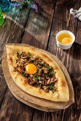 Adjarian khachapuri adorned with mushrooms and a bright egg yolk, served on a rustic wood backdrop