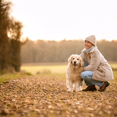 Woman Stroking Golden Retriever Dog On Walk Around Field In Autumn Countryside