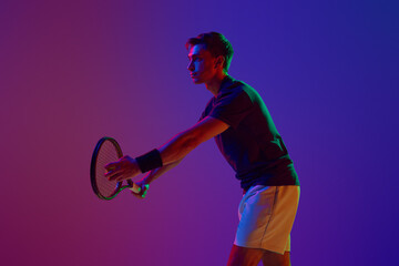 Competitive man in his 30s, tennis player in motion, serving ball with racket, practicing against...