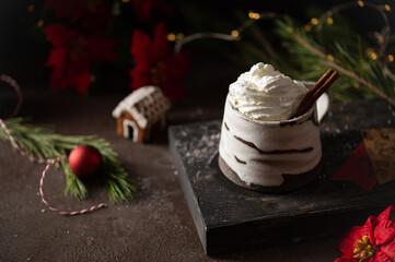 Hot winter drink in a clay mug. Close-up of hot chocolate with cinnamon stick, gingerbread house. Winter cozy still life with cocoa, Christmas decorations, fir branch and lights. © Lizaveta