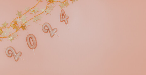 Candle numbers 2024 with festive gold star garland on pink.