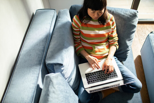 Woman on sofa using typing laptop at home