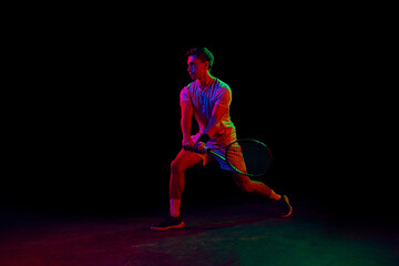 Fototapeta na wymiar Young man, tennis player during game, playing, practicing against dark background in neon light. Concept of professional sport, competition, game, math, hobby, action