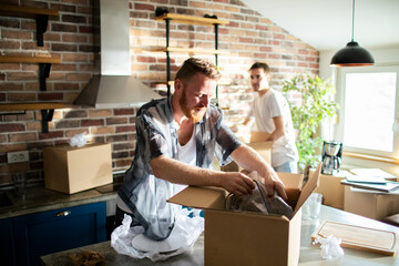 Young male gay couple unpacking boxes at new home - obrazy, fototapety, plakaty