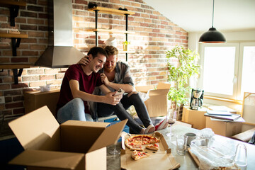 Happy gay couple eating pizza in new home