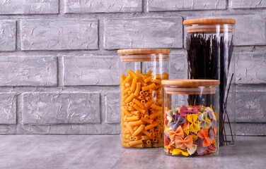 Storing pasta of three types in glass jars against the gray brick wall. Food storage in a pantry