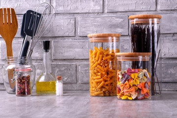 Storing pasta of three types in glass jars against the gray brick wall. Food storage in a pantry