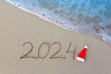 New Year 2024 background with Santa hat and handwritten in the white sand.