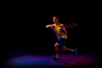 Fototapeta na wymiar Concentrated athletic man, tennis player in motion, training, practicing against dark background in neon light. Concept of professional sport, competition, game, math, hobby, action