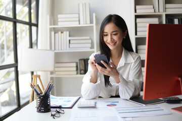 Asian businesswoman in formal suit in office happy and cheerful during using smartphone and working