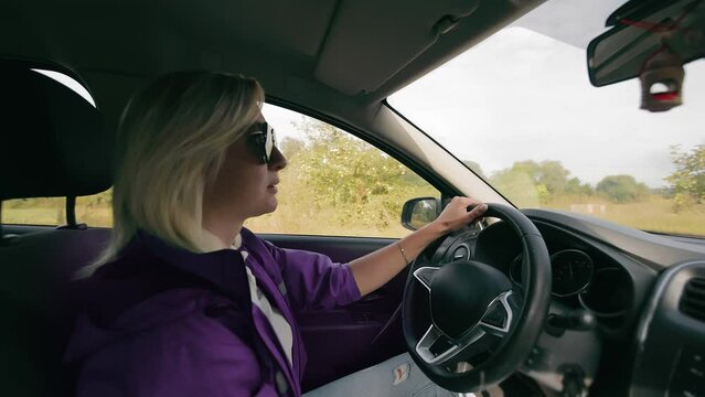 Driver on Rural Road, Woman driving a car on a rural road in a purple jacket is driving on a rural road. View from the passenger's side to the driver.
