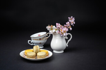 Still life with pistachios and orange macaroons arranged with beautiful fine porcelain in baroque style on a black background