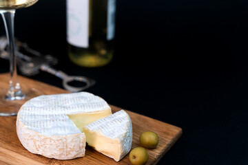 Camembert cheese, olives and wineglass of white wine on a dark background. Close-up. Copy space. Selective focus.