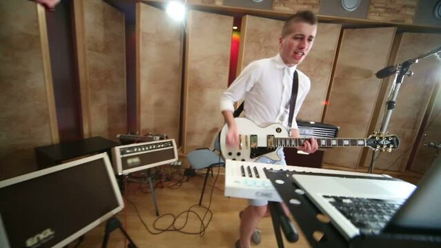 Woman sings to microphone and guy play guitar in Studio 