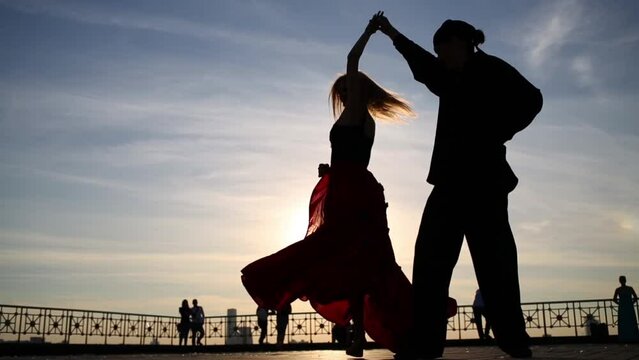 Silhouette of graceful young couple dancing outdoor against sky