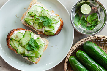 fresh and healthy vegetable appetizer cucumber toast with greek yoghurt mint and basil on a grey minimal concrete background