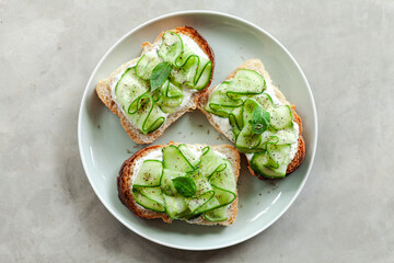 fresh and healthy vegetable appetizer cucumber toast with greek yoghurt mint and basil on a grey minimal concrete background