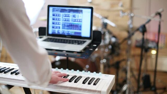 Back of man playing keyboard and laptop in recording studio