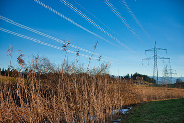 High voltage power lines in a rural area against a blue sky, background snow-capped mountains....