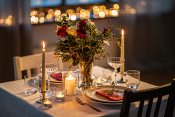 holidays, romantic date and celebration concept - close up of festive table serving for two with flowers in vase and candles burning at home on valentine's day - 694978759