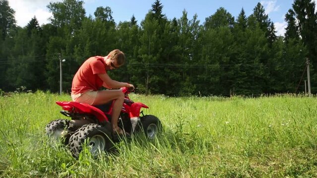 Man in sunglasses rides, turns and slows on red quad bike