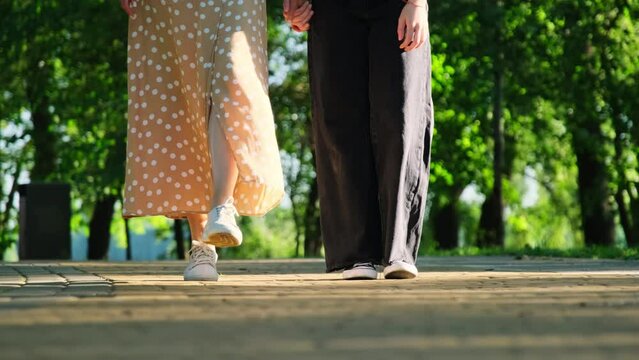 Approaching mother and teenage daughter figures wearing canvas shoes on paved road. Family stops on lane in park in closeup